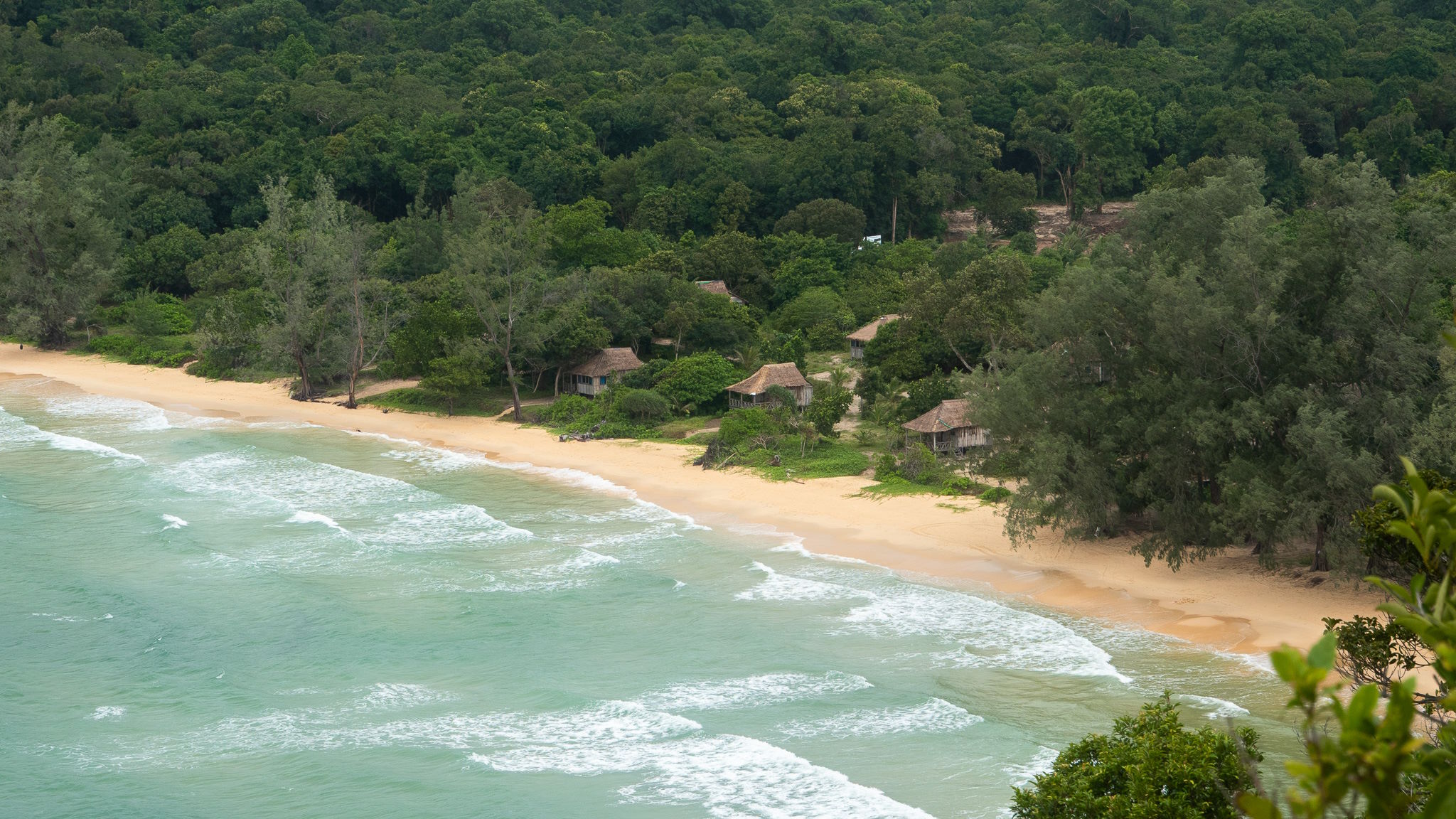 vue sur la Lazy Beach de haut, vagues et cabanes en bois entourées d'arbres